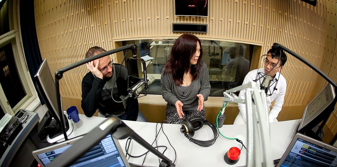 Fish-eye shot of three people sitting and talking together at a radio station.